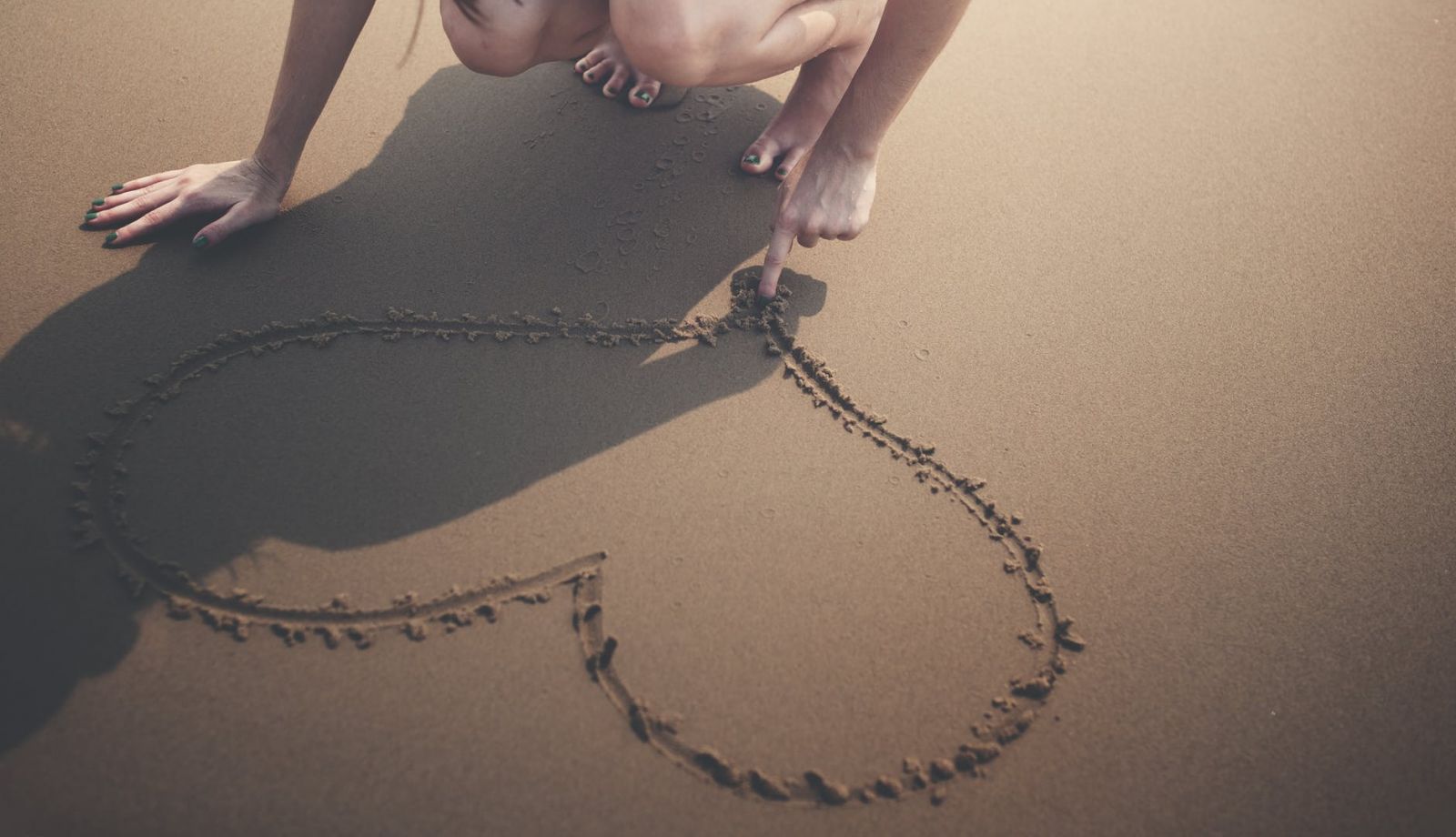 Devojka crta srce u pesku 